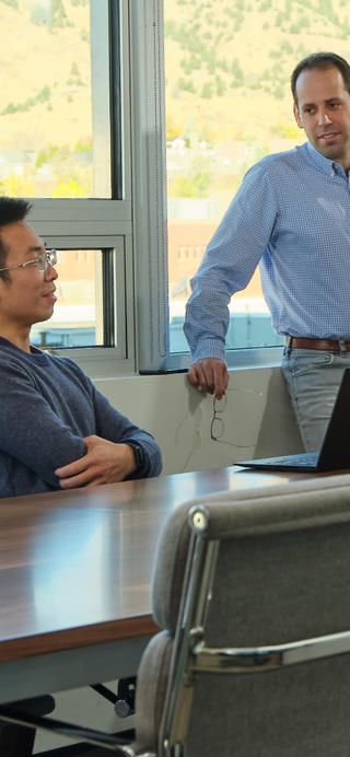 Two men at a conference table with a window in the background.