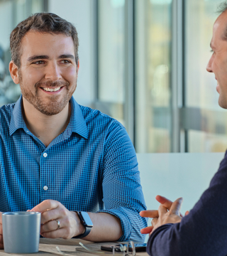 A man in a blue shirt talking with a man in a dark blue sweater.