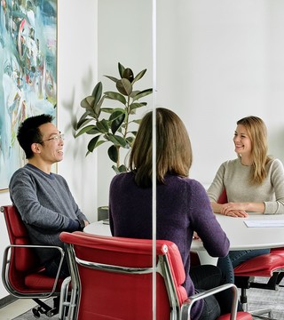 Two men and one woman sitting around a round conference table in red leather chairs.